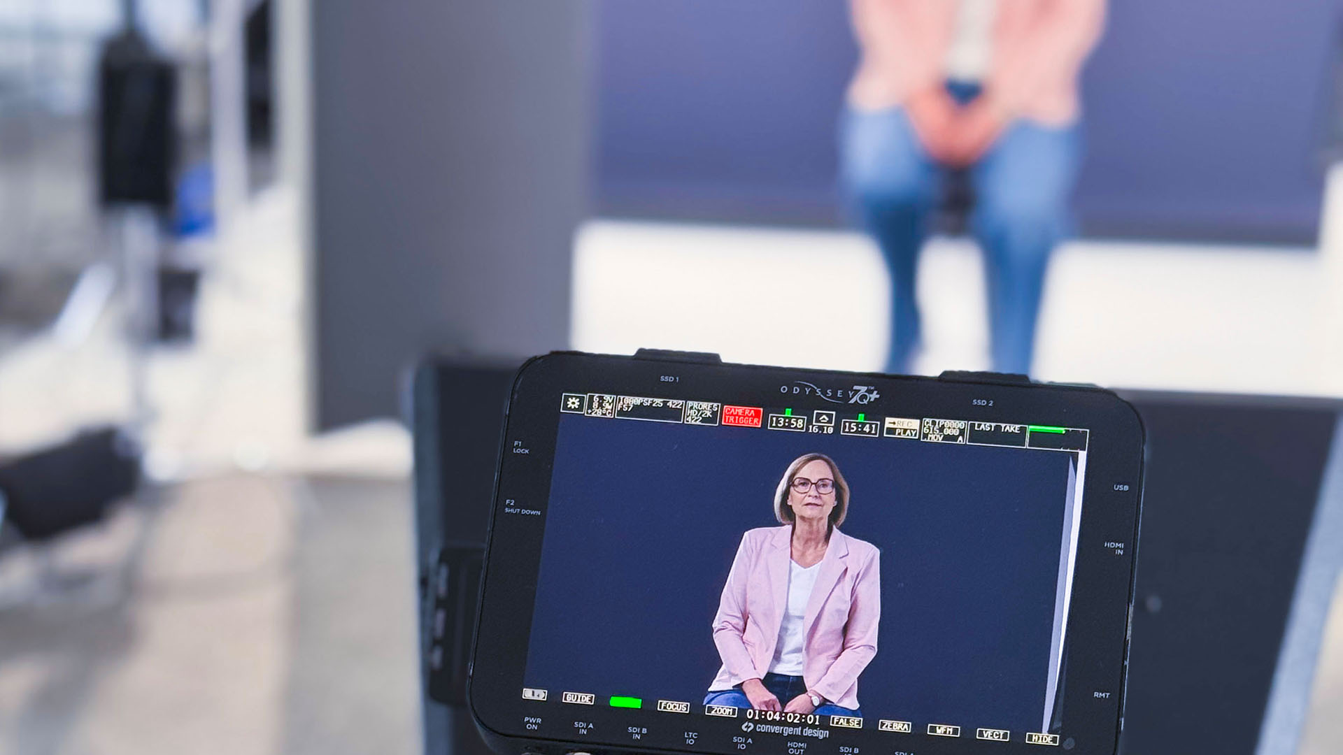 Frau sitzt im Filmstudio vor blauem Hintergrund, gefilmt über den Kameramonitor.