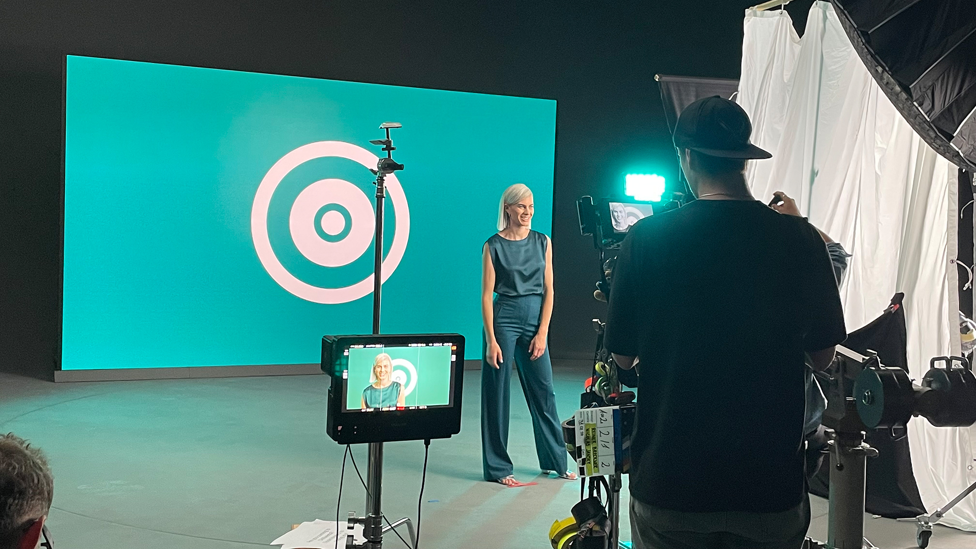 Videoproduktion im Studio: Frau vor großem Display, Kamerateam im Vordergrund.