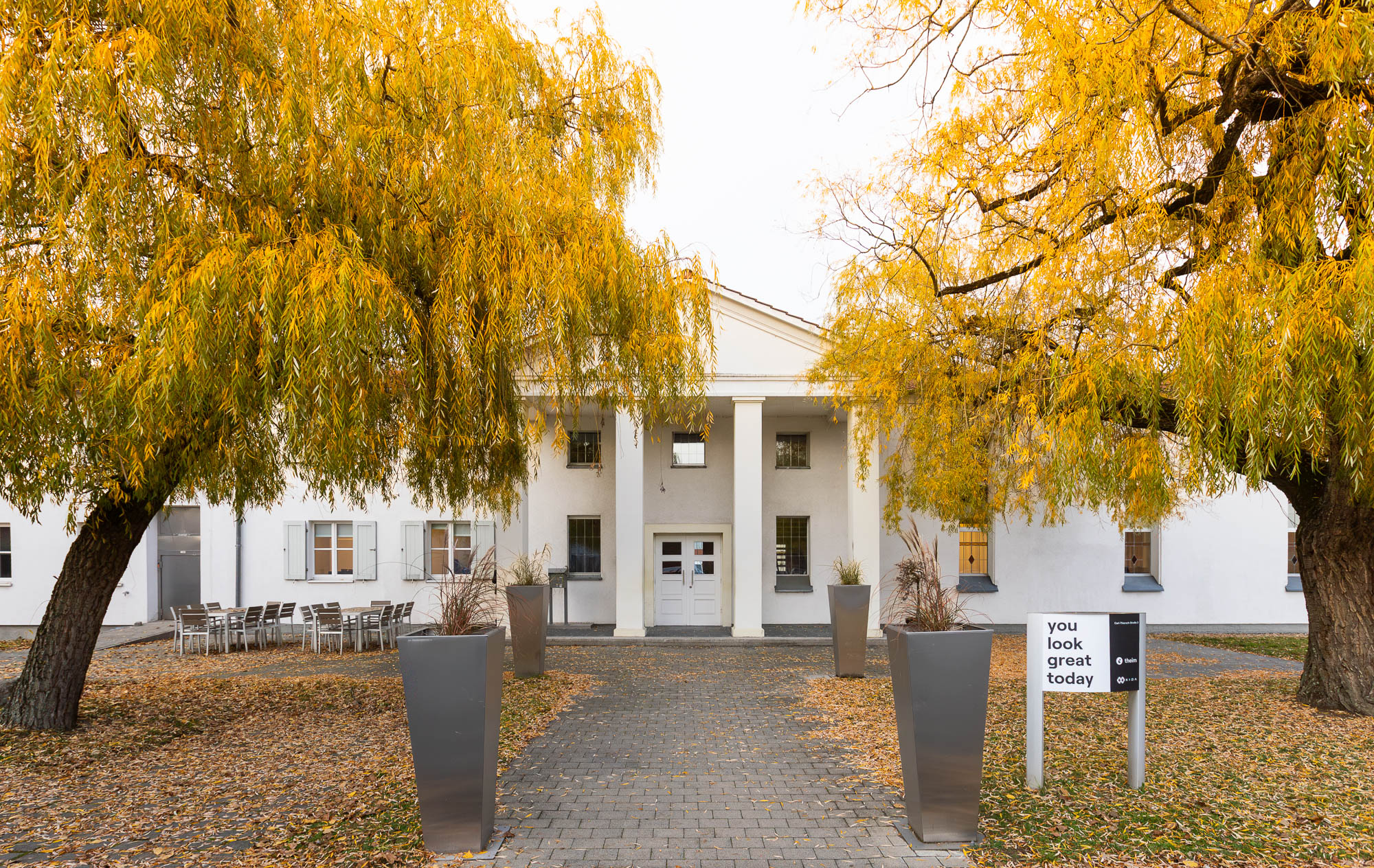 White agency building with columns and autumn trees in the courtyard.